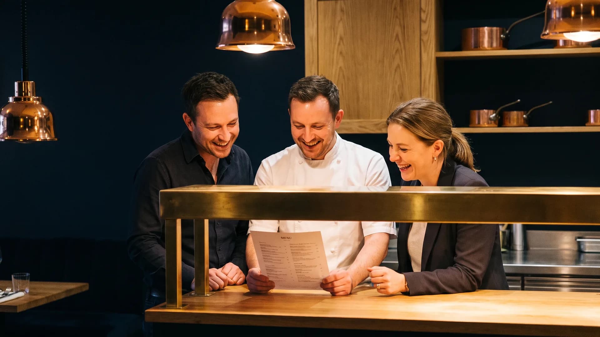A restaurateur, a chef and a floor manager reviewing a menu at the pass