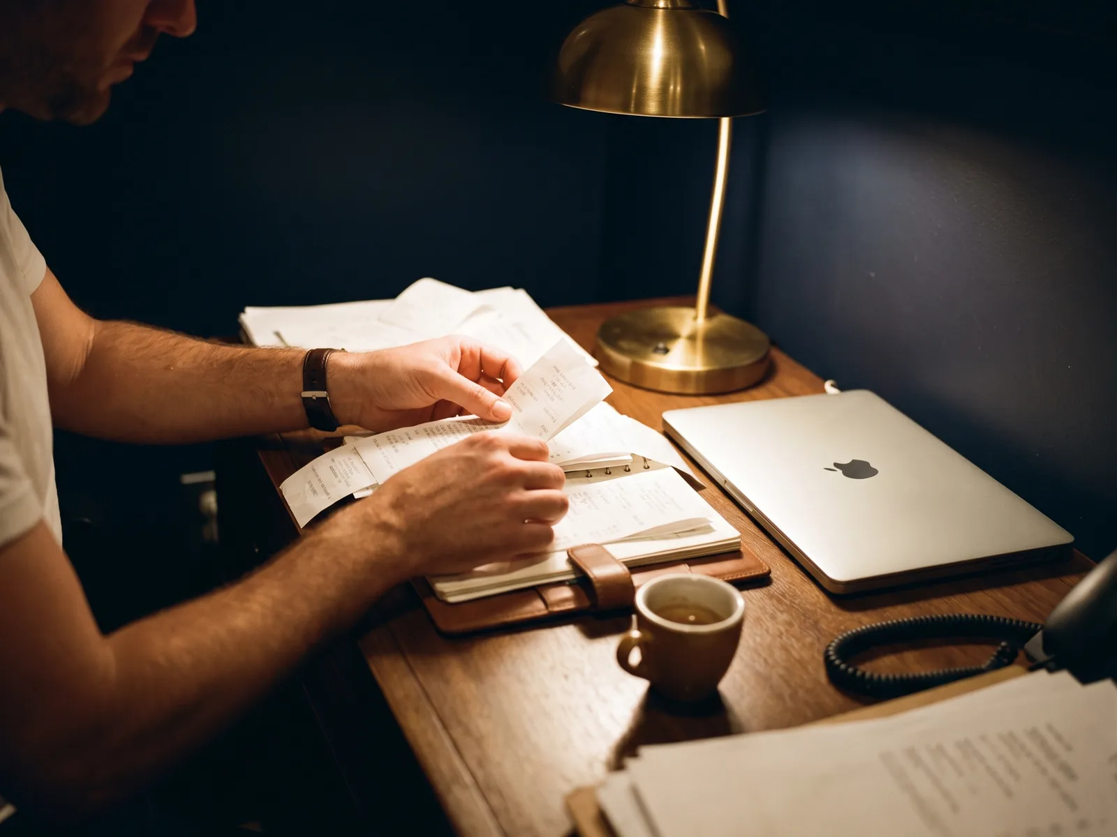 A manager sorting receipts under a desk lamp during the end-of-night close
